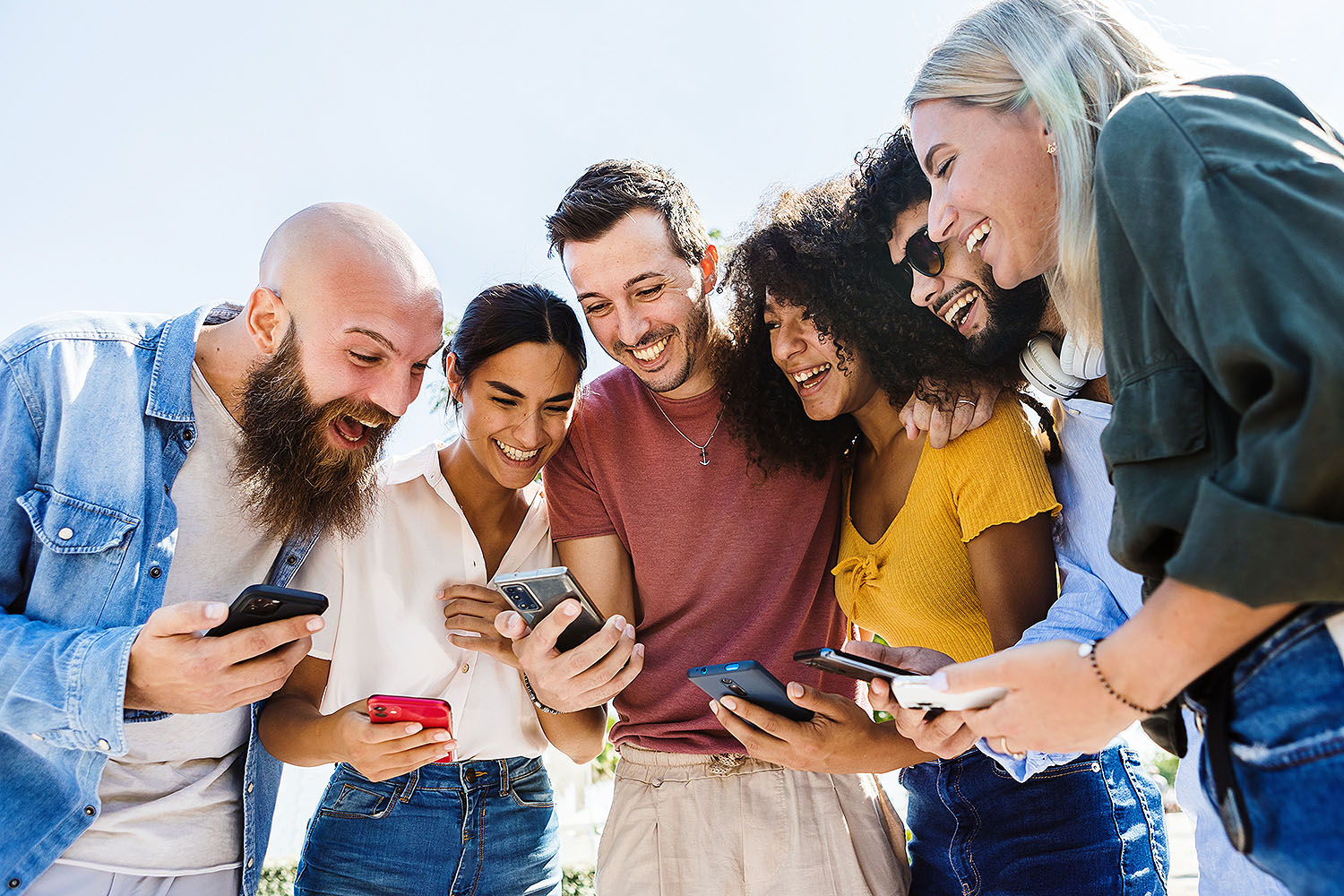 Young group of happy people smiling while using mobile phone together outdoors